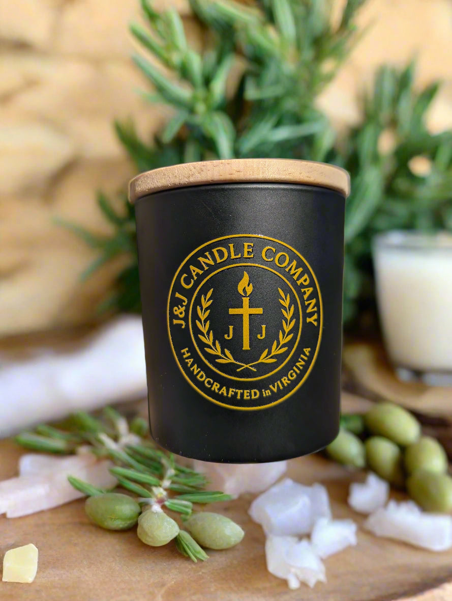 Black candle with a wooden lid featuring the J & J Candle Company logo on a brick surface.