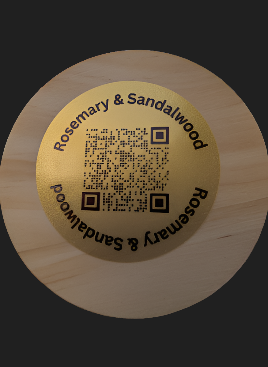 Round wooden candle lid with 'Rosemary & Sandalwood' branding and QR code on a dark background